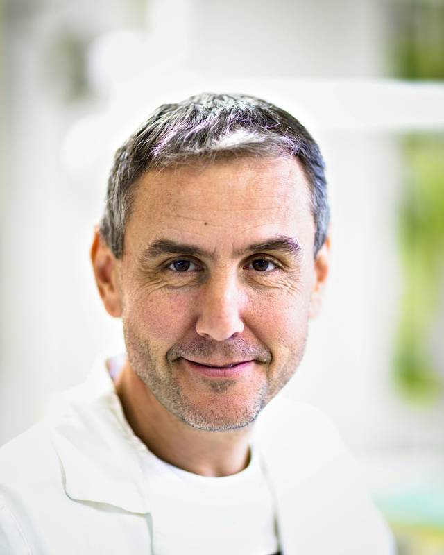 Retrato del Dr. Andrés Navarro, hombre de pelo canoso y barba corta, sonriendo con bata blanca.