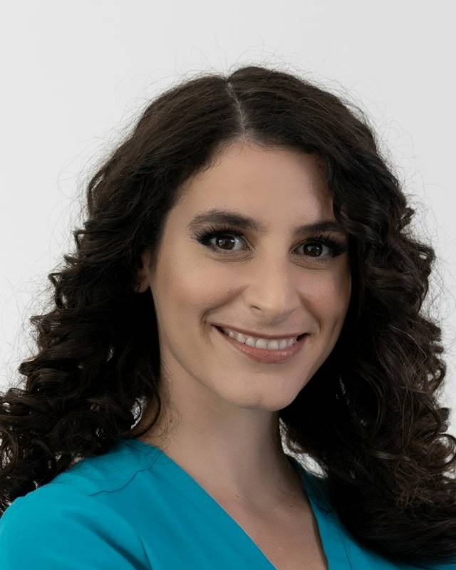 Retrato de la Dra. Laura Ferrer, mujer de pelo largo rizado y oscuro, sonriendo con pijama sanitario turquesa.