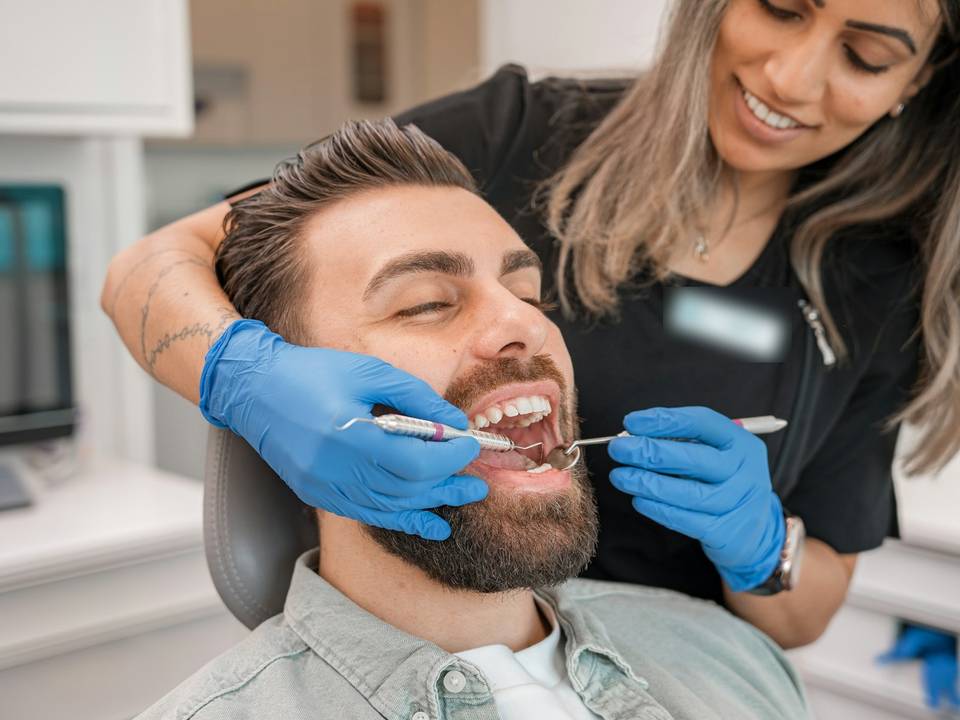 Una dentista revisa la boca de un paciente sonriente recostado en el sillón dental.